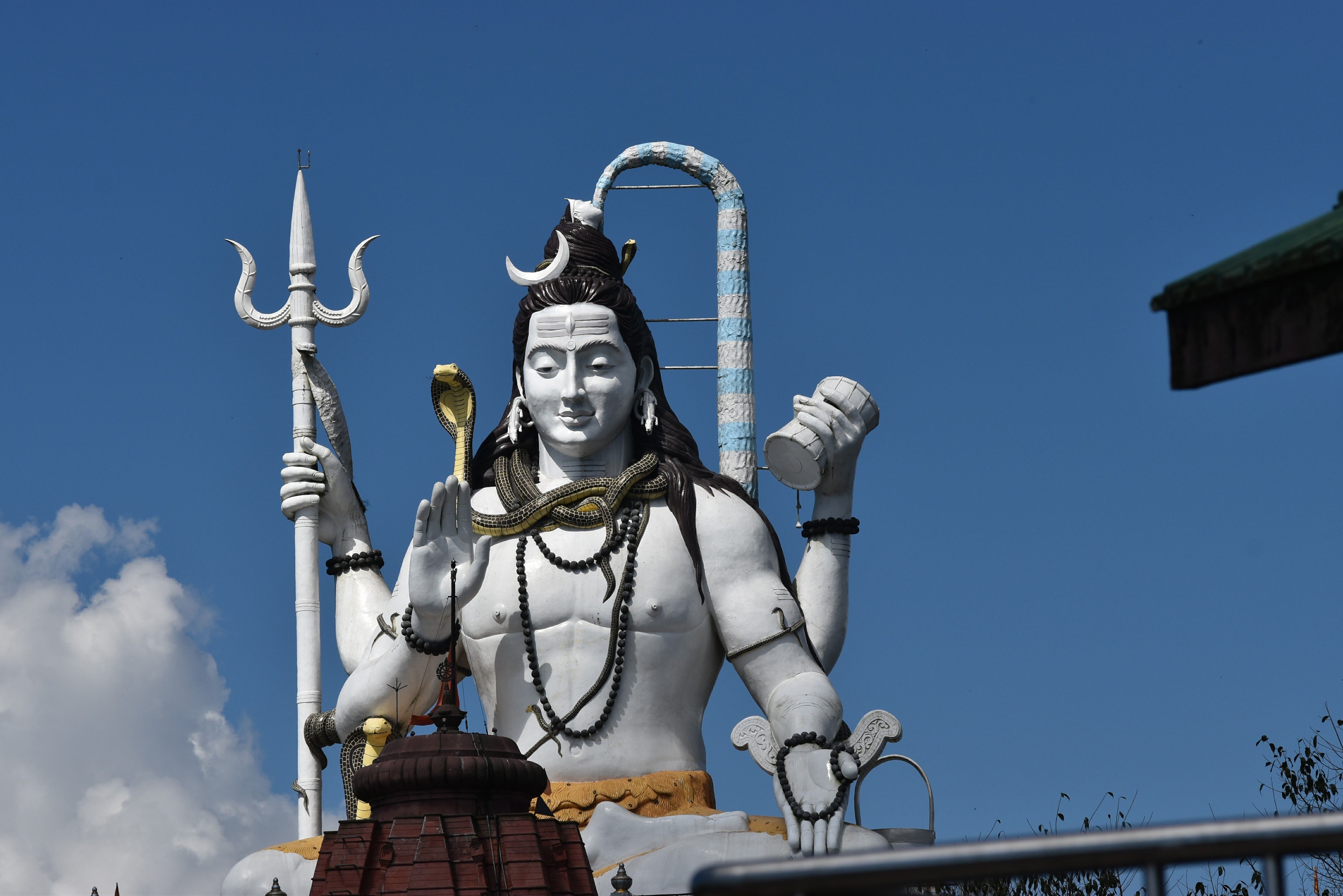 Majestic statue of Lord Shiva with trident and cobra against a clear blue sky, epitomizing serenity and divinity.