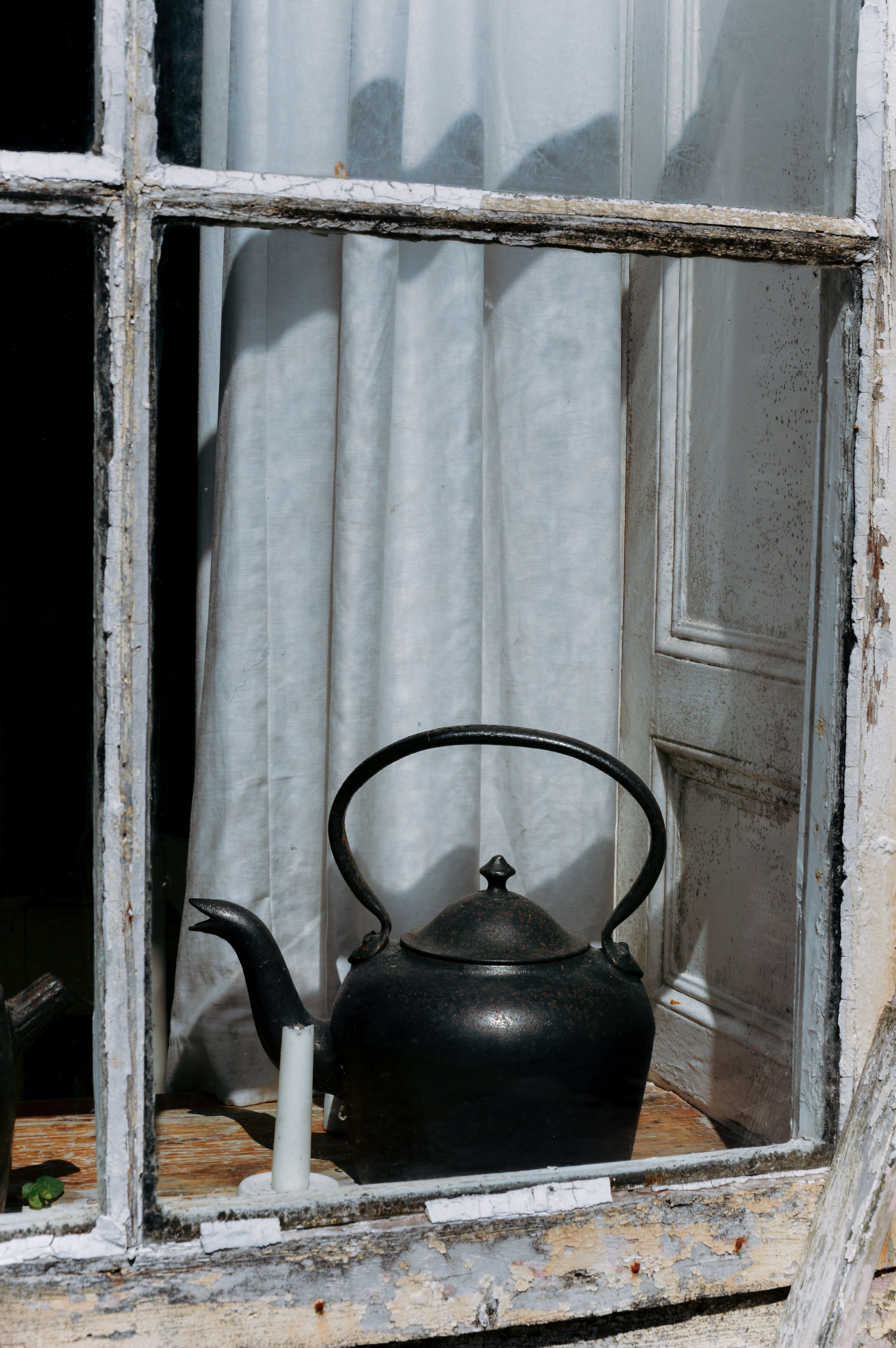 A rustic teapot sits by a window with peeling paint, inside an Irish cottage.