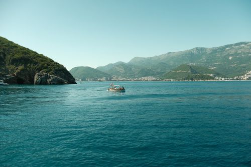 Free Serene view of a boat on the Adriatic Sea with Montenegro's coastal mountains in the background. Stock Photo