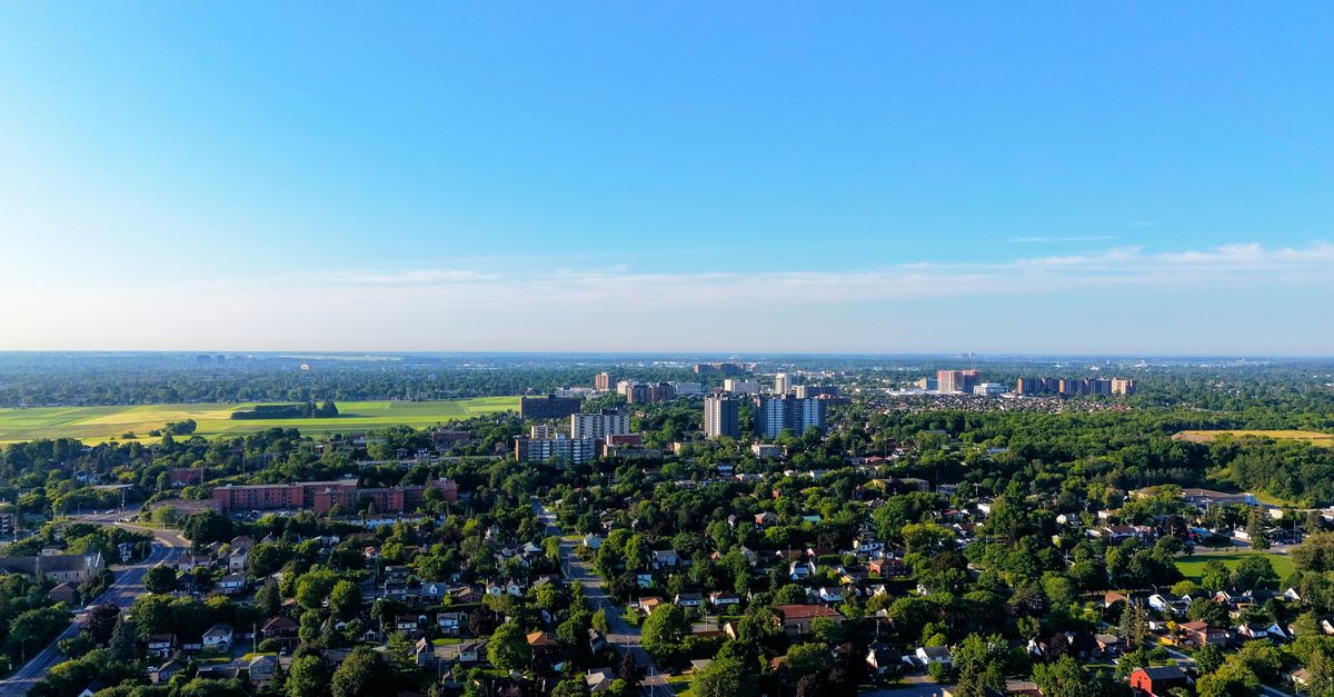 Aerial view of cityscape with residential and green areas under a clear blue sky.