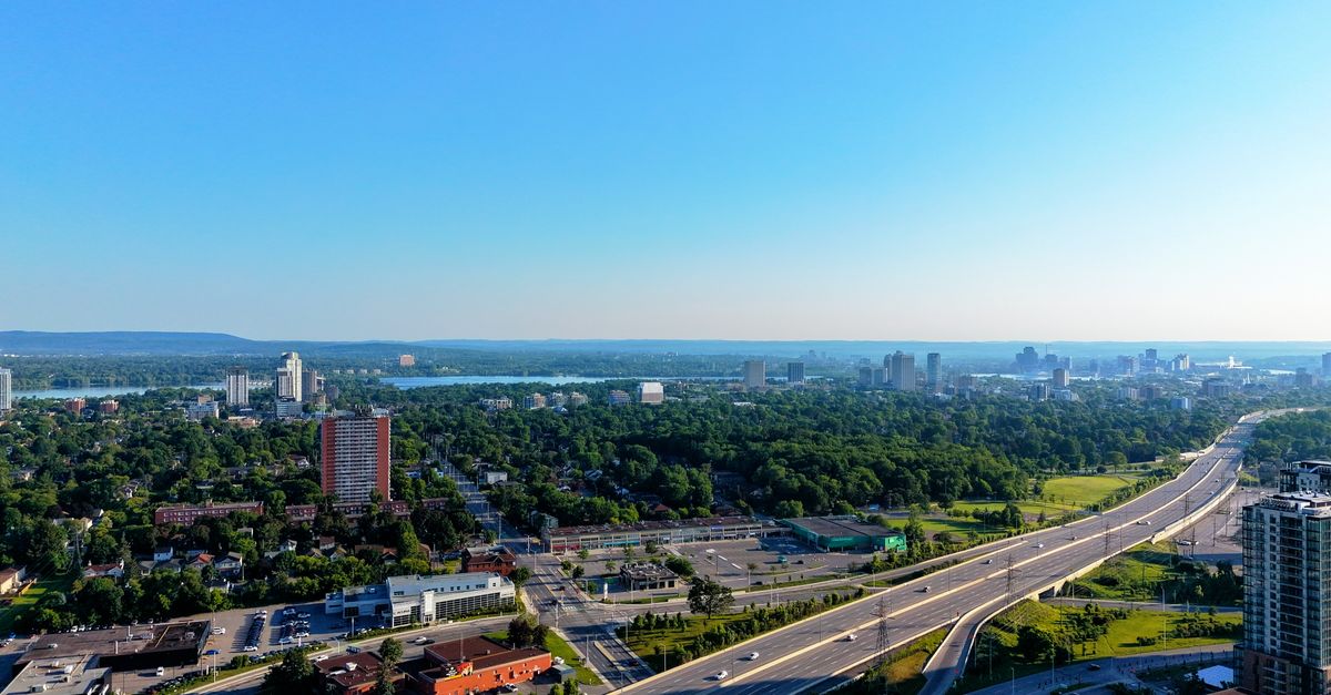 Aerial view of a cityscape with skyscrapers and a highway under clear blue skies.