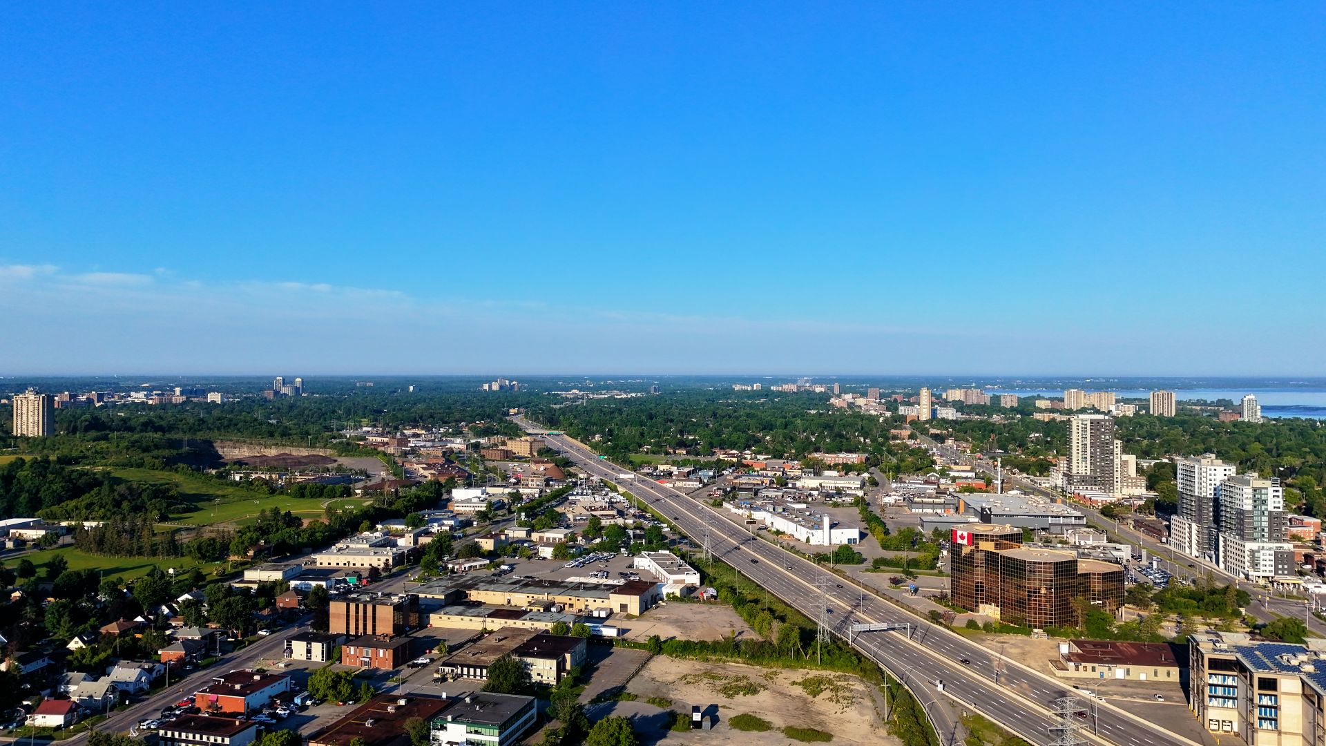 Aerial view of a cityscape with highway, buildings, and greenery under a clear blue sky.