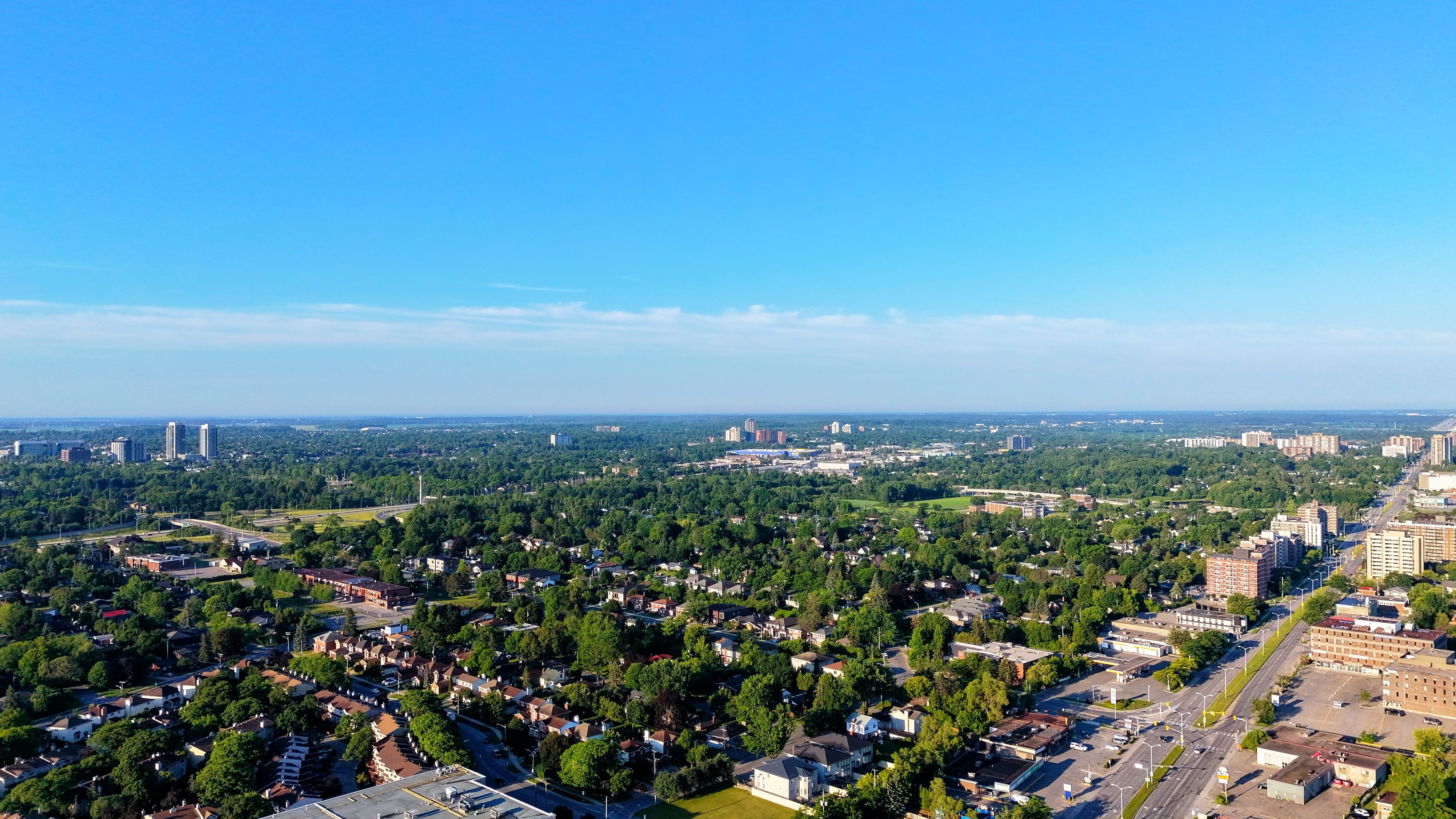 Aerial view of a sprawling suburban area with lush greenery and buildings under a clear blue sky.