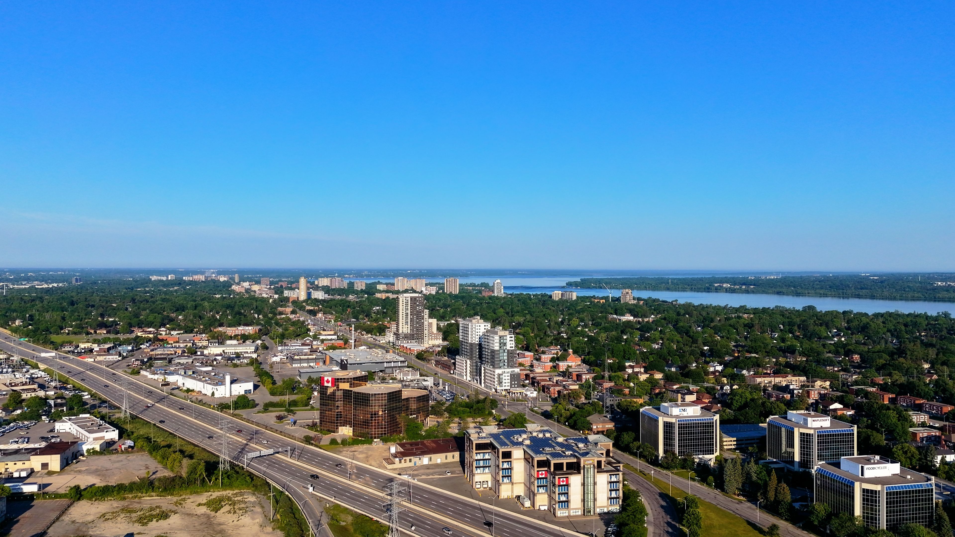 Outstanding 45 mins Helicopter Tour to Mt Assiniboine & its Glaciers in Banff Review 2026 - Aerial photograph of a Canadian city with a highway, buildings, and greenery under a bright blue sky.
