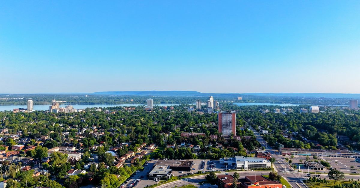 A stunning aerial view of a cityscape with river, urban areas, and lush forests under a clear blue sky.