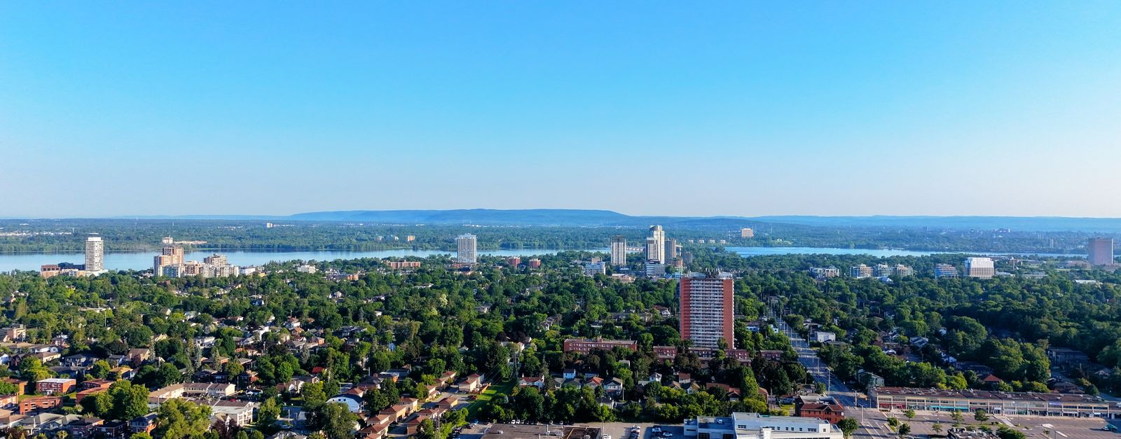 A stunning aerial view of a cityscape with river, urban areas, and lush forests under a clear blue sky.