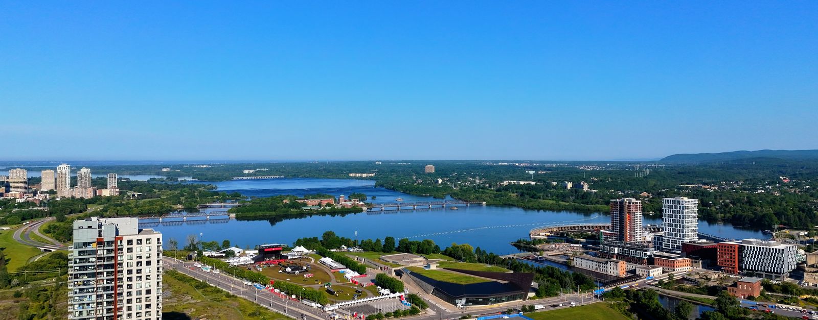 Aerial shot capturing a vibrant cityscape alongside a serene river under a clear blue sky.