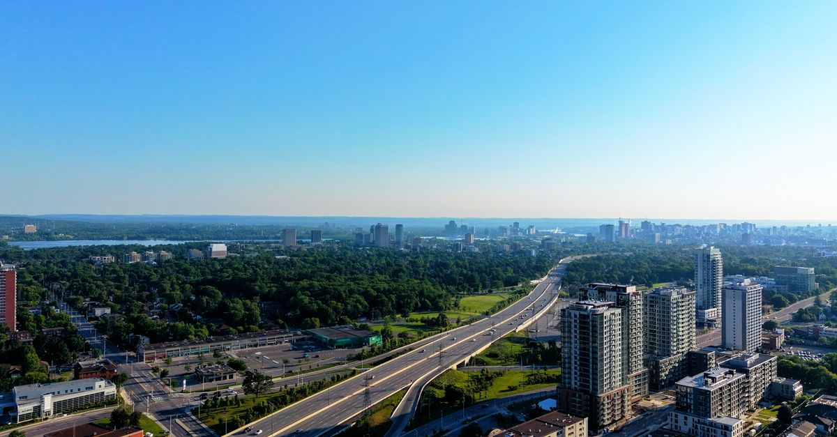 Aerial photograph of a city skyline with highways and greenery under a clear blue sky.