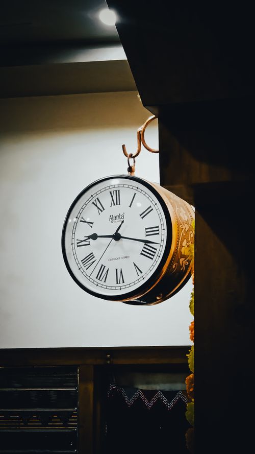 Free Elegant vintage wall clock mounted indoors with Roman numerals, creating a classic ambiance. Stock Photo