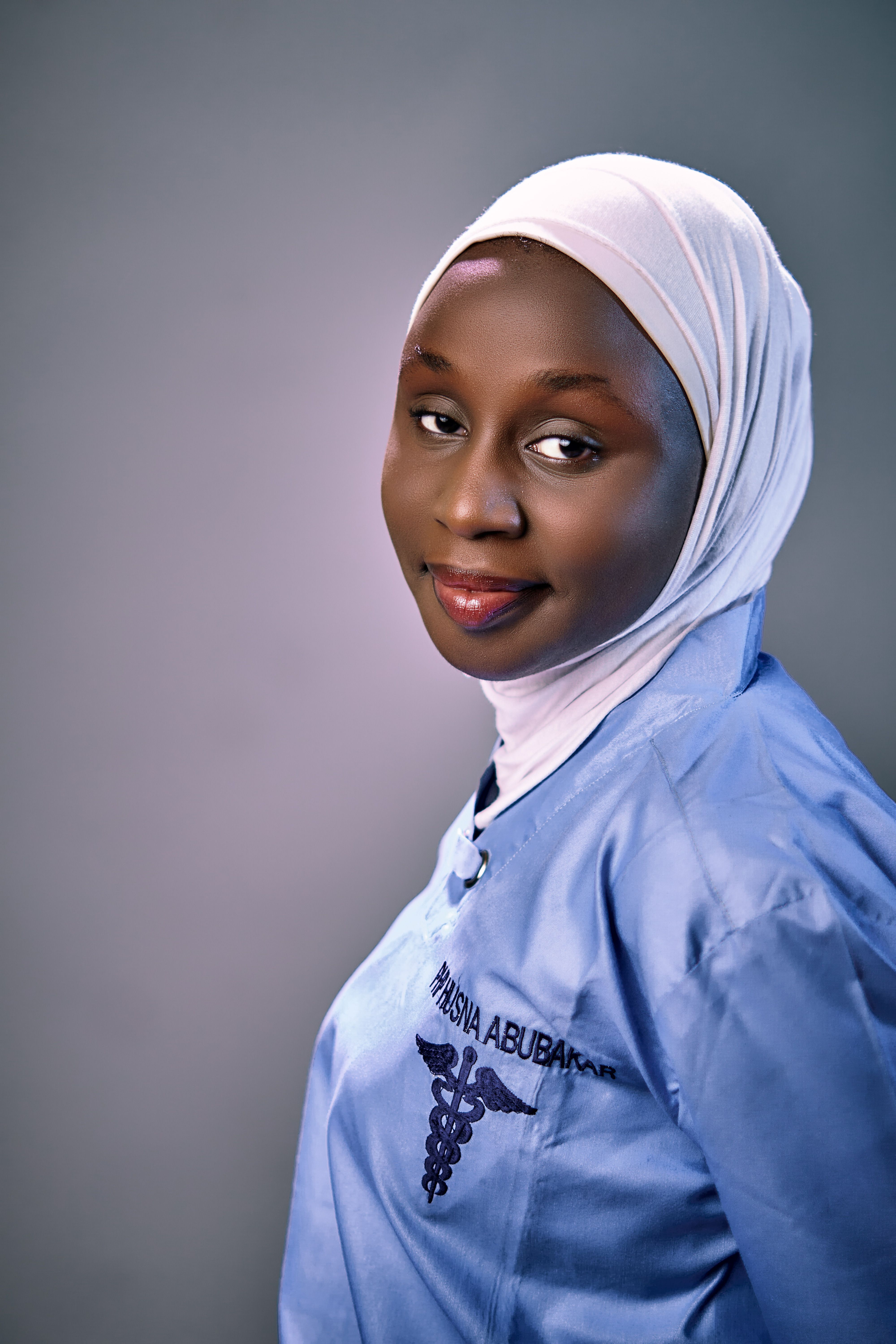 Portrait of a woman in a medical uniform and hijab, smiling.