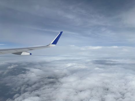 A stunning aerial view from an airplane with a blue wingtip soaring above fluffy white clouds.