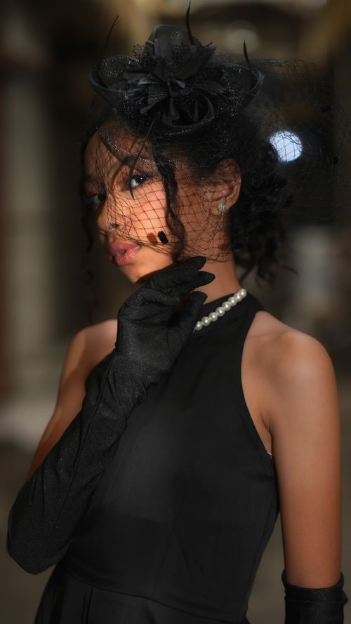 Free Sophisticated woman in black dress and gloves, posing indoors with elegant hat and veil. Stock Photo