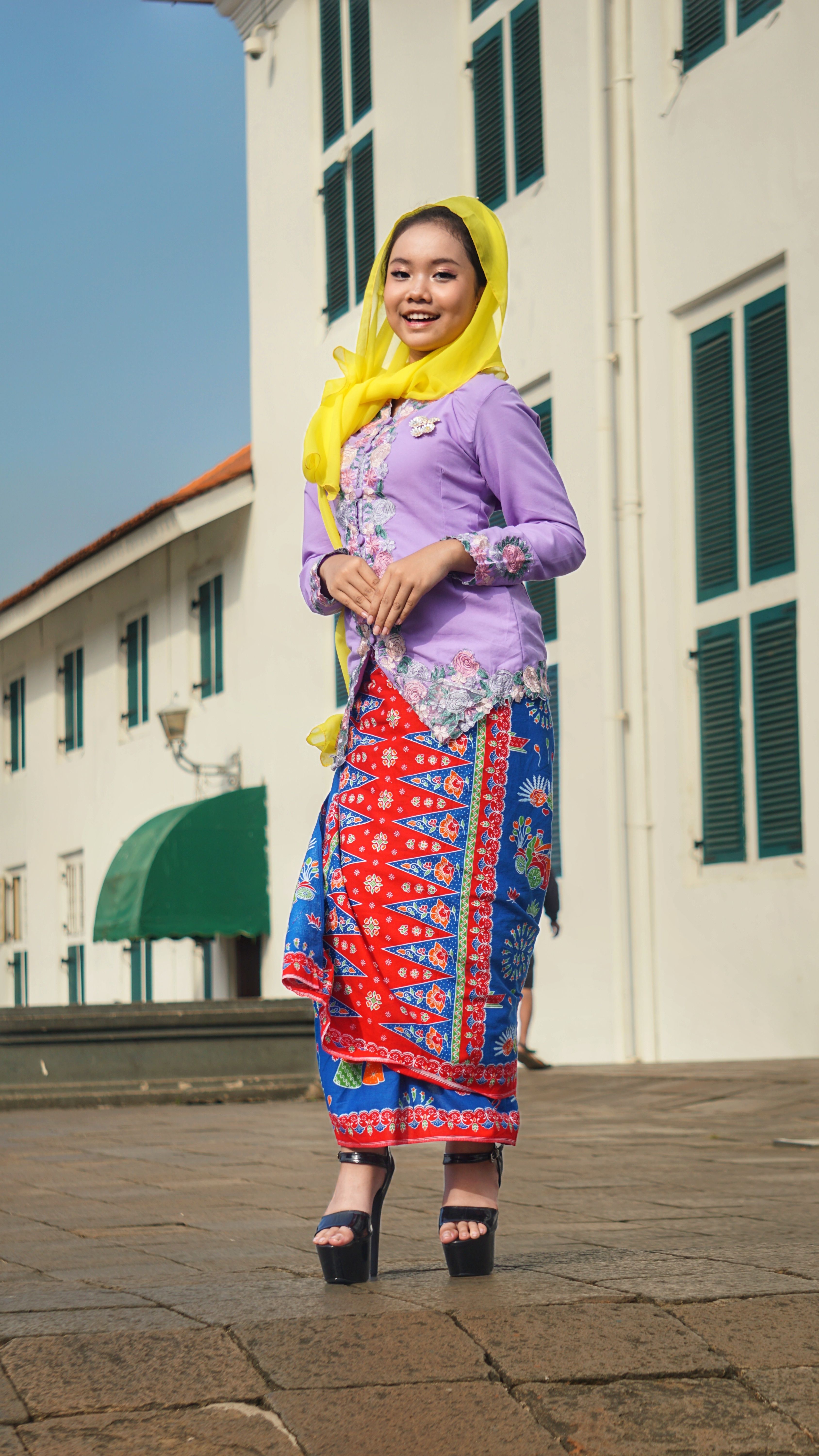 Woman in colorful traditional attire poses in front of historic Jakarta building.