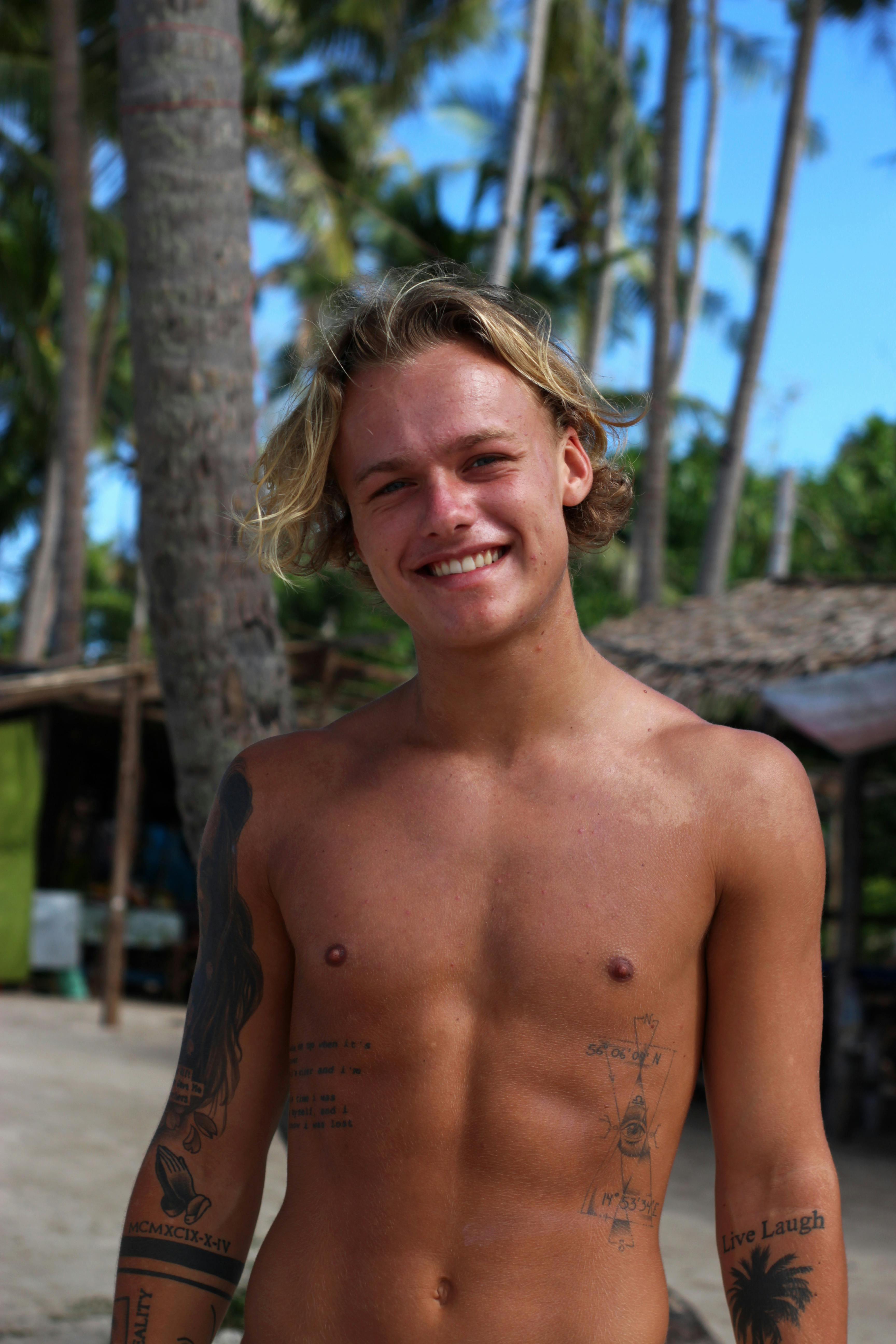 一个光着膀子、开朗的男人，在海滩上纹着身，享受着阳光明媚的一天