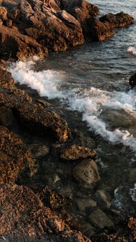 Captivating view of sunset waves crashing on a rocky shoreline in İzmir, Türkiye.