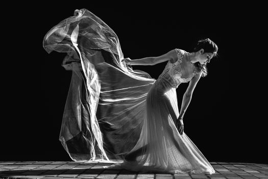 An elegant bride gracefully poses in a flowing dress, contrasting against a dark background.