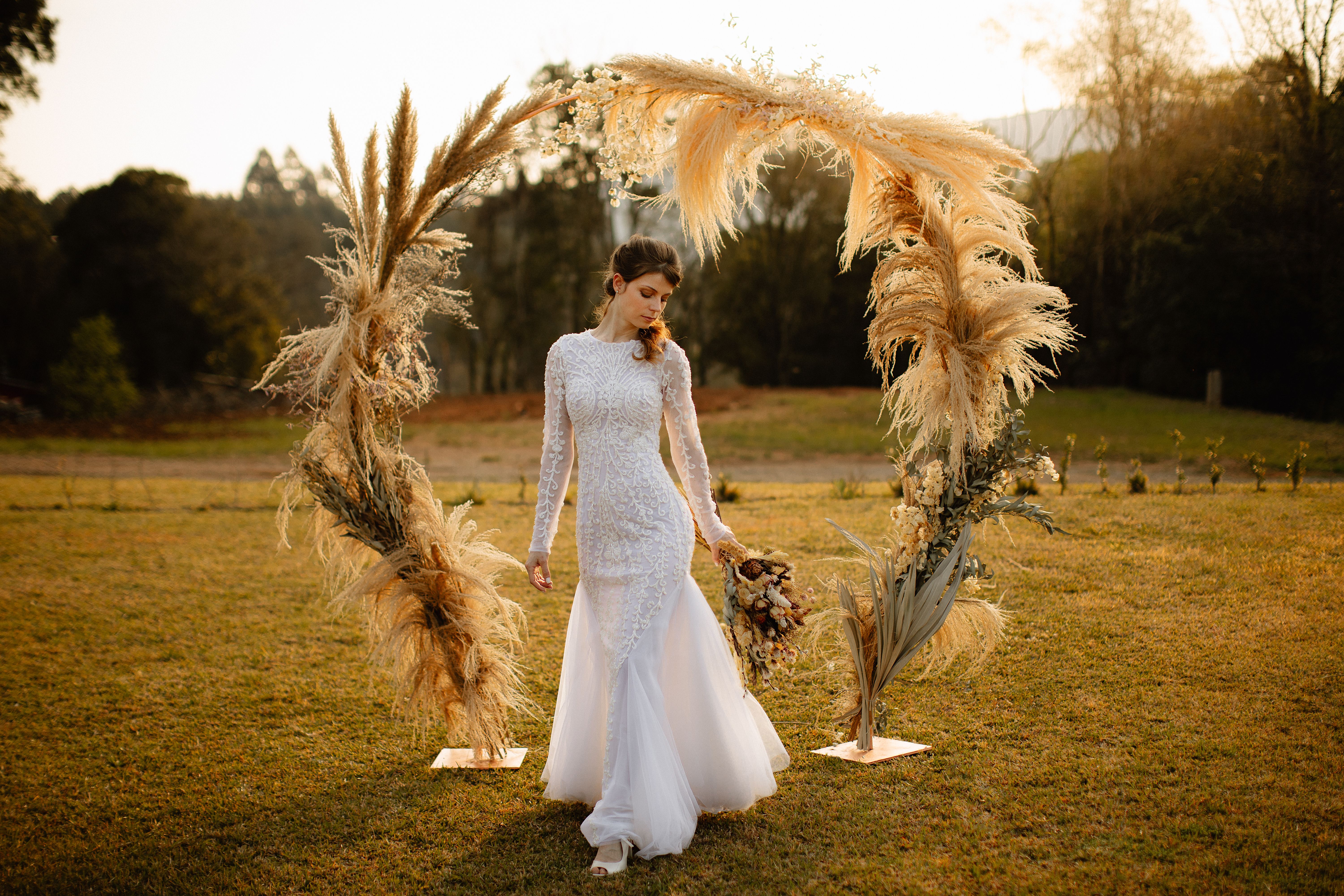 A beautiful bride in a white lace dress poses outdoors at sunset in Gramado, Brazil.