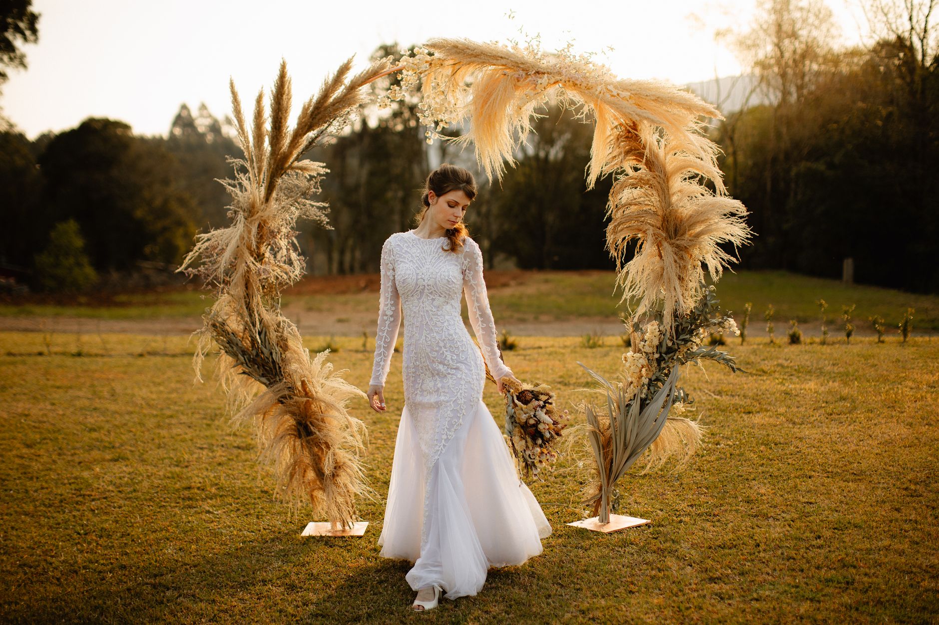 A beautiful bride in a white lace dress poses outdoors at sunset in Gramado, Brazil.