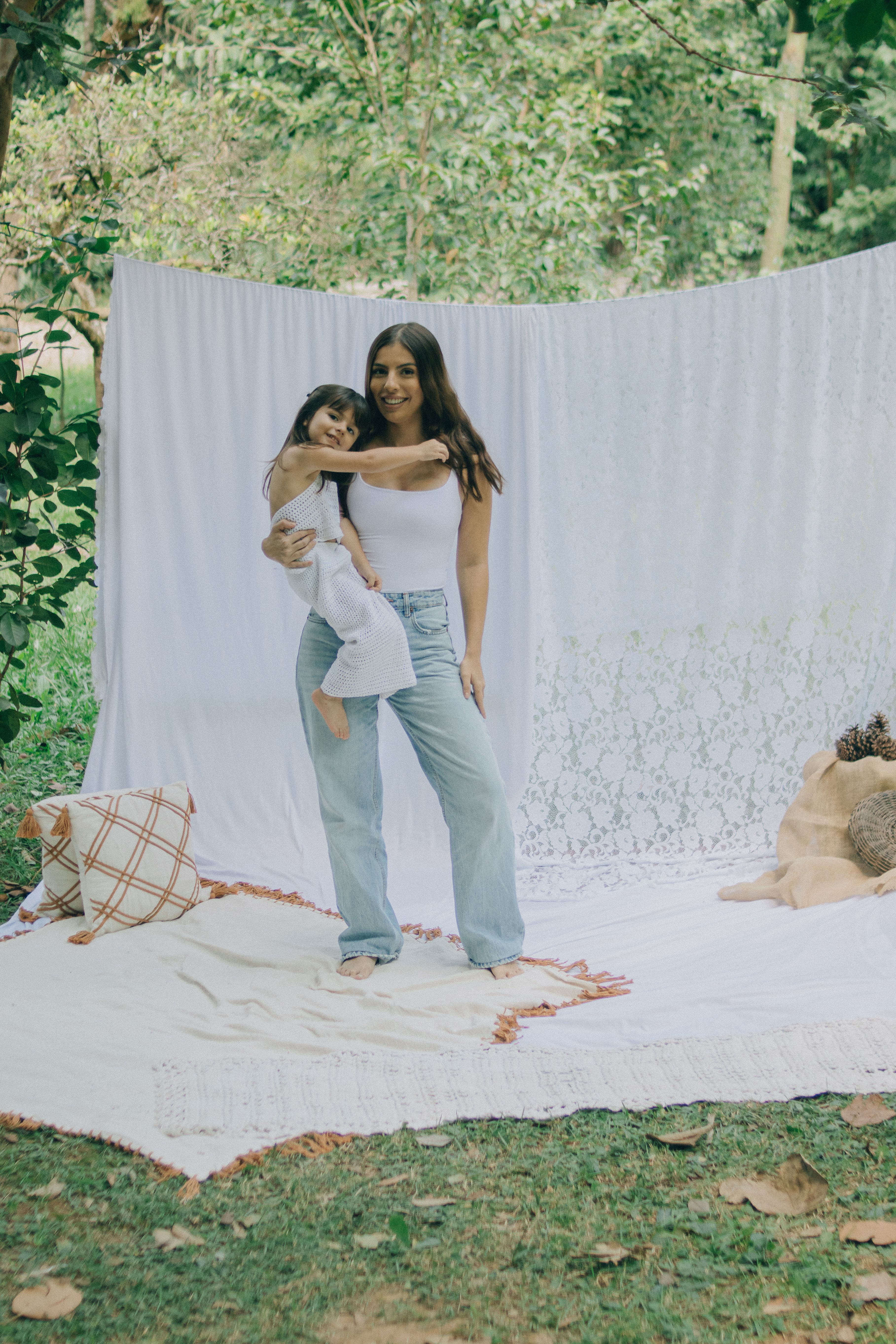 A serene portrait of a mother holding her child outdoors with white fabric backdrop.