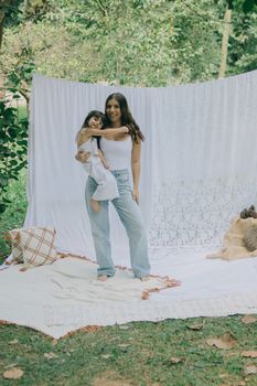 A serene portrait of a mother holding her child outdoors with white fabric backdrop.