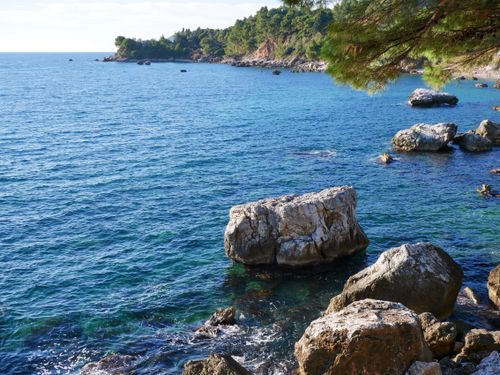 Free A serene coastal scene with clear blue water and rocky shoreline under a sunny sky. Stock Photo