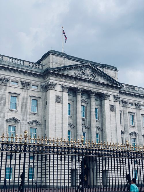 Free A view of Buckingham Palace with its iconic facade and gold-trimmed gates under a cloudy sky. Stock Photo