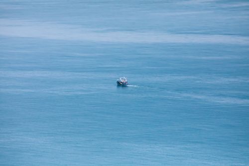 Free A solitary fishing boat navigates the expansive, calm blue ocean on a clear day. Stock Photo