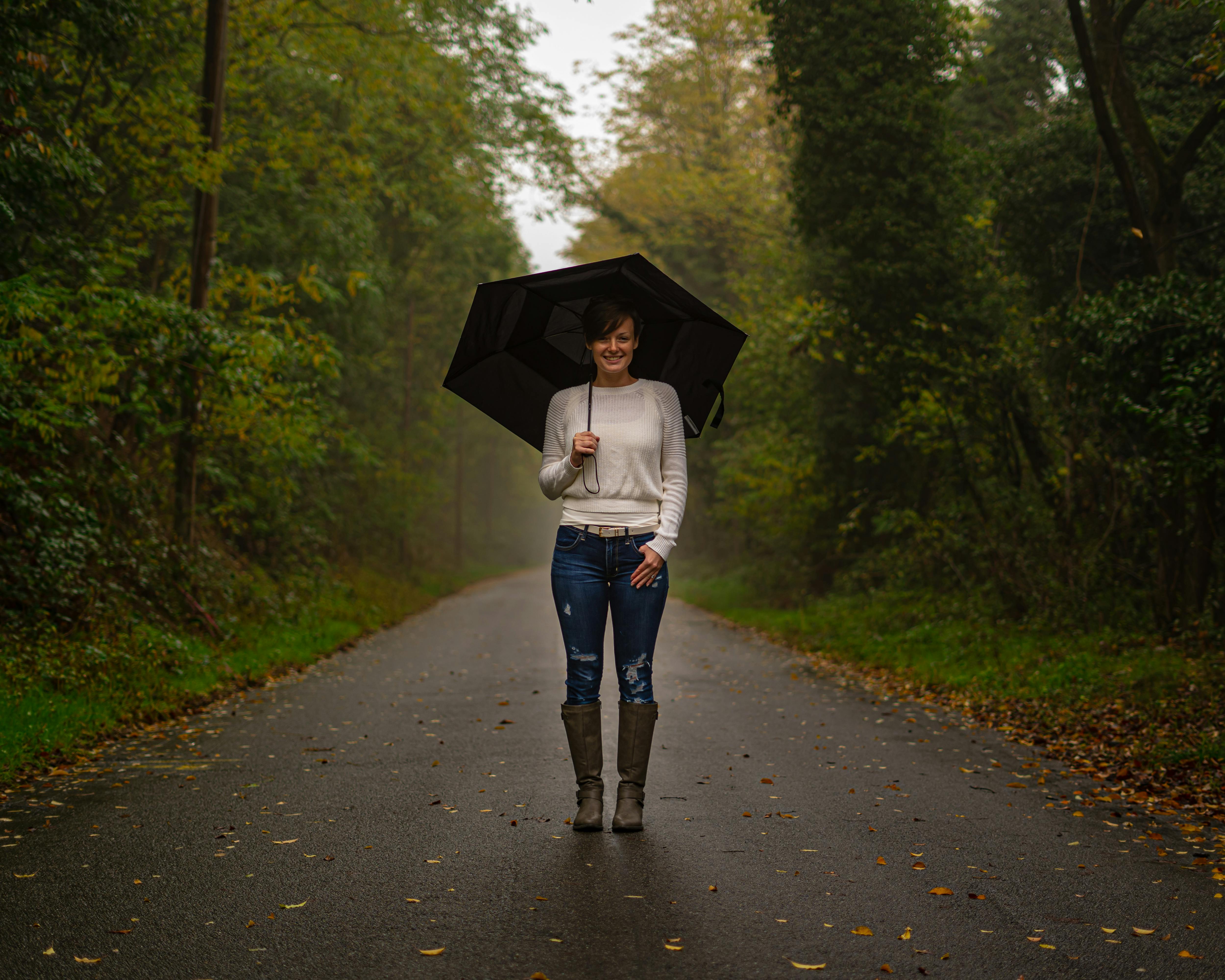 woman in white top and blue denim jeans holding umbrella walking on road