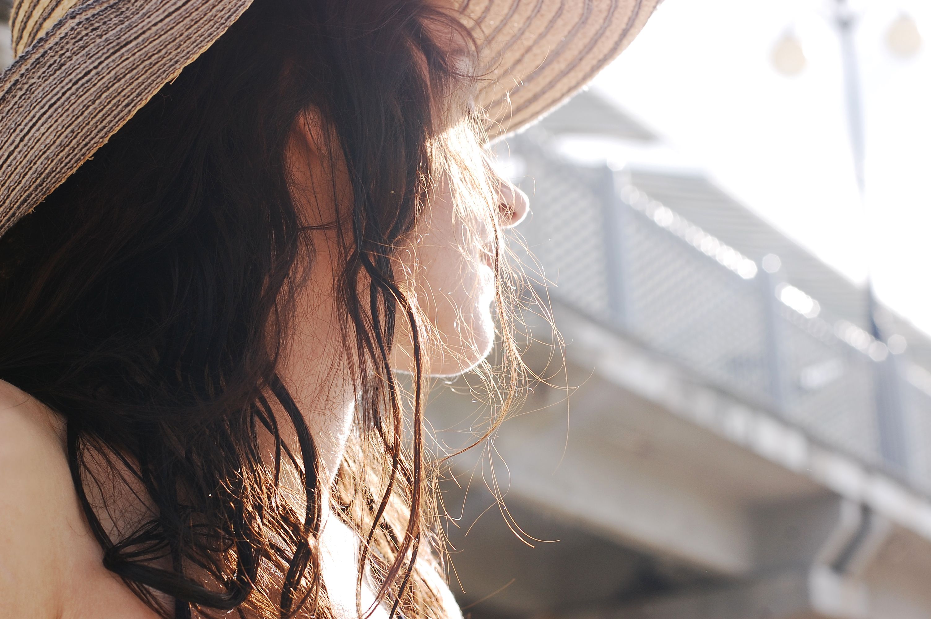 A woman in a straw hat enjoying the warm sun, with a blurred urban background and a sense of relaxation.