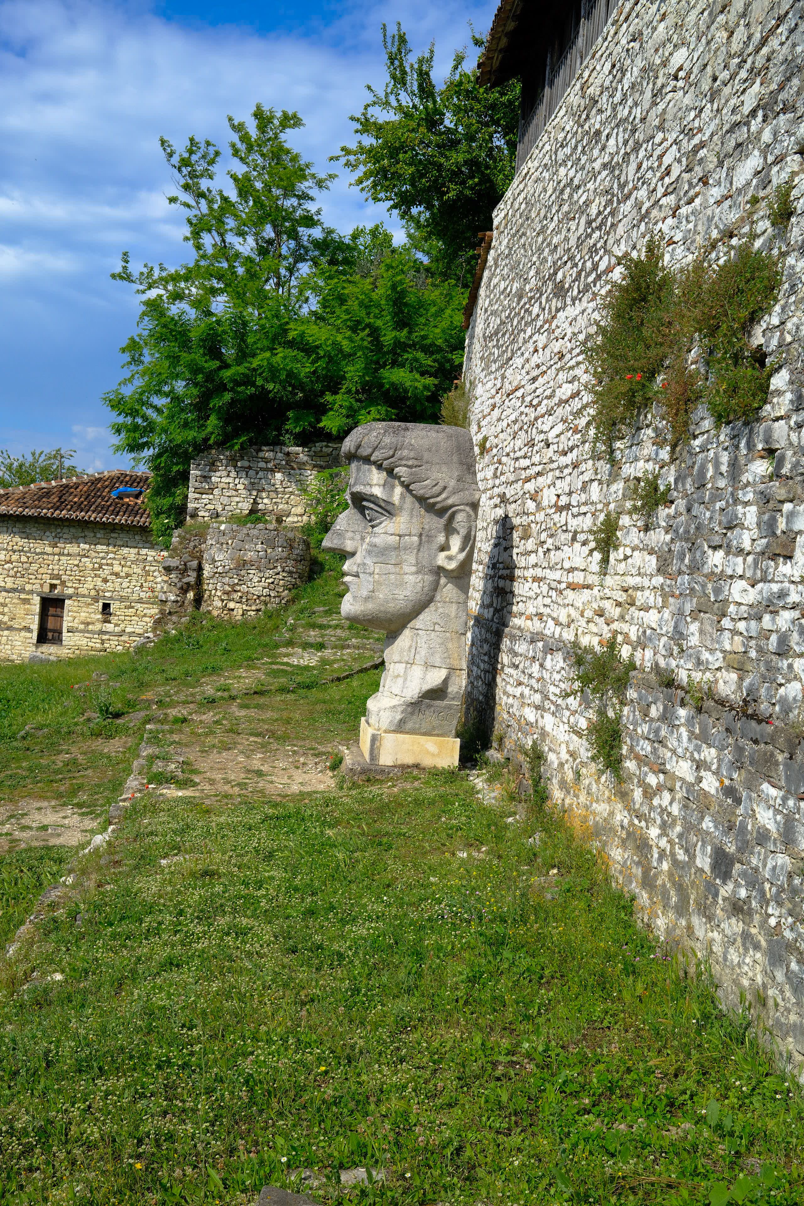 Large stone sculpture of a face beside an ancient stone wall outdoors in daylight.