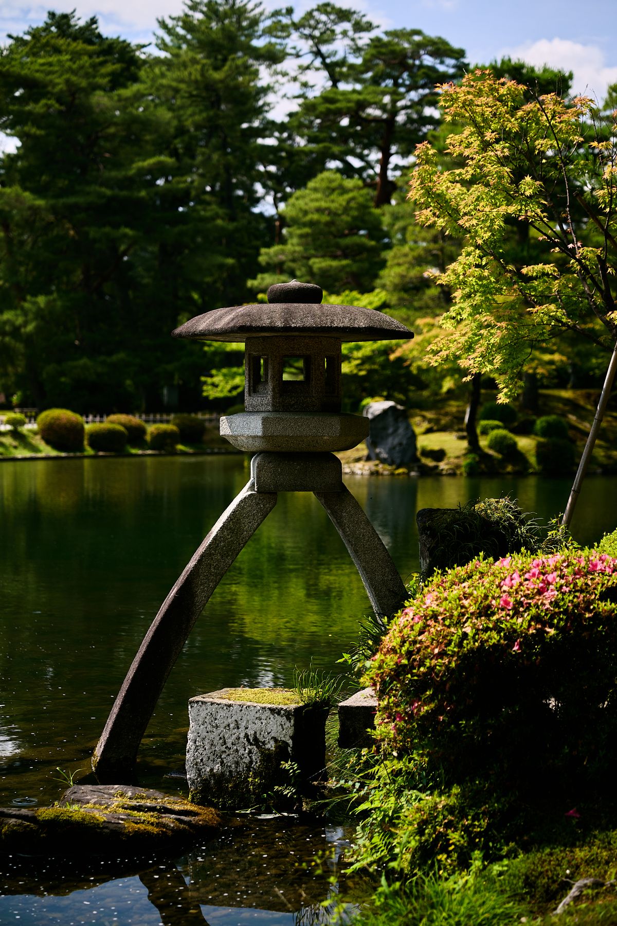 Two-legged stone lantern beside a pond in Kenrokuen Garden, Kanazawa, surrounded by pines and azaleas
