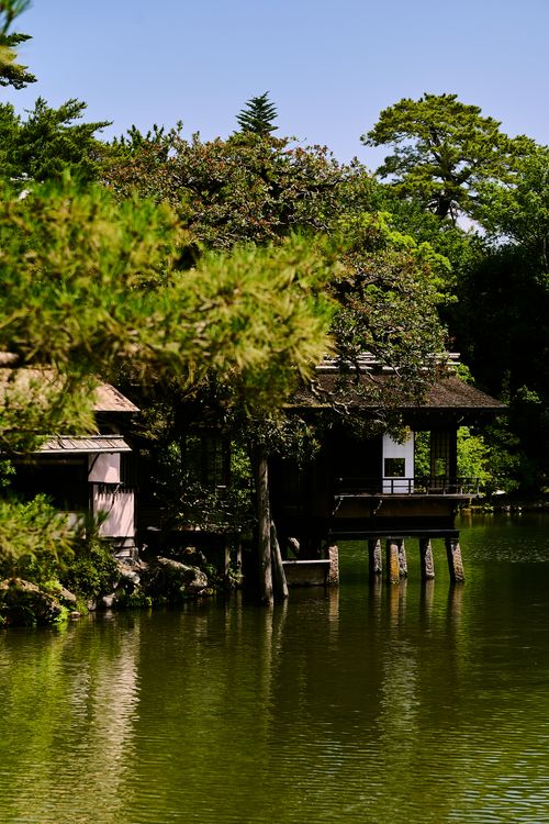 Free Serene view of a traditional Japanese tea house surrounded by lush greenery and a calm lake in Kanazawa. Stock Photo