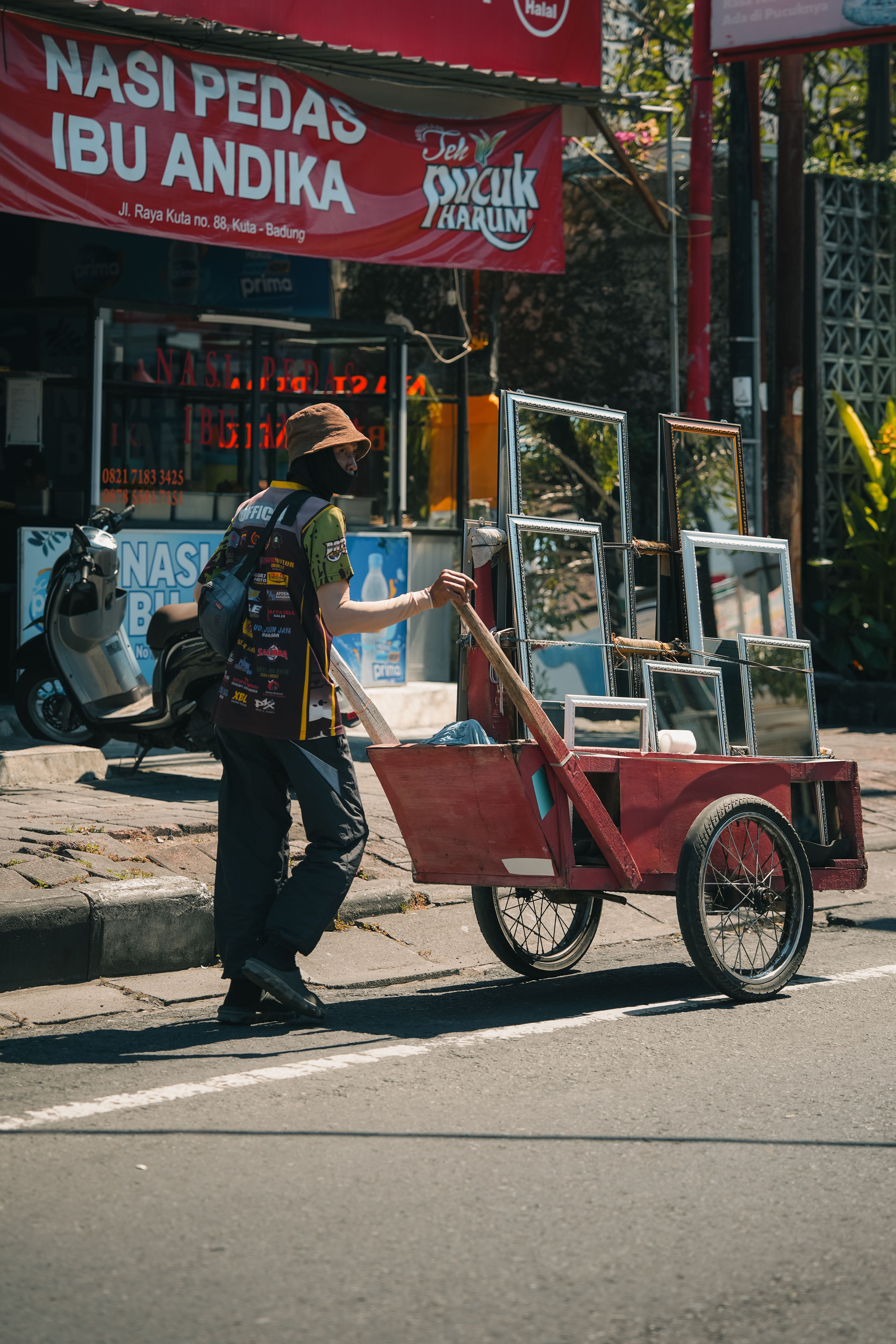 Outdoor scene of a street vendor pulling a wooden cart loaded with mirrors in a lively urban setting.