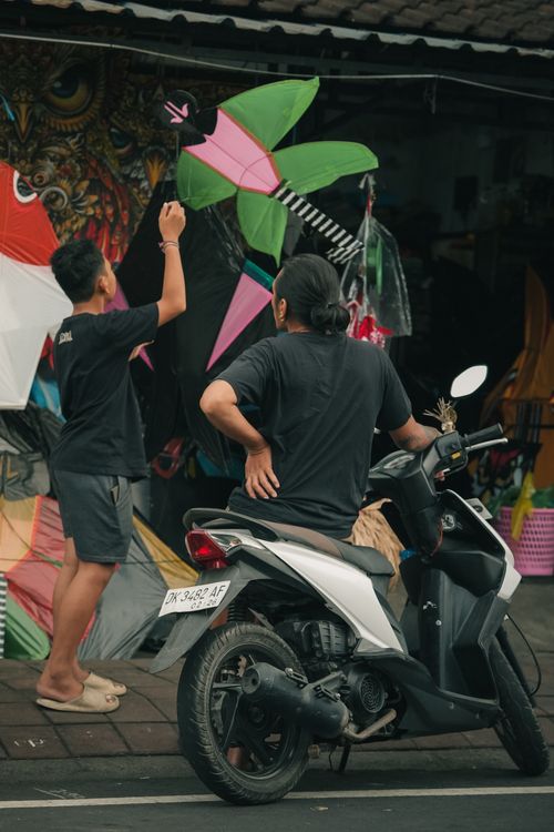 Free Two people admire colorful kites on display outside a market, adding a lively splash to the scene. Stock Photo
