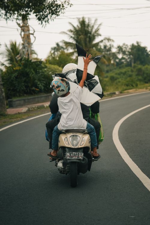 Free A child with a kite rides with an adult on a scooter along a rural road. Stock Photo