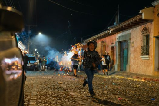 Joyful celebration with fireworks and people on a cobblestone street in Antigua Guatemala at night.