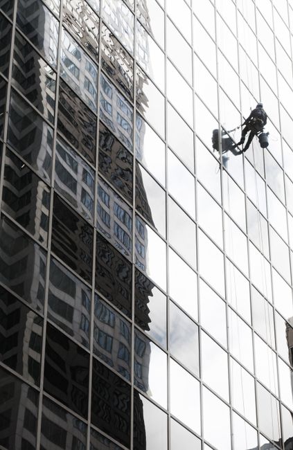 A window cleaner works on a high-rise building facade in Chicago, reflecting the cityscape.