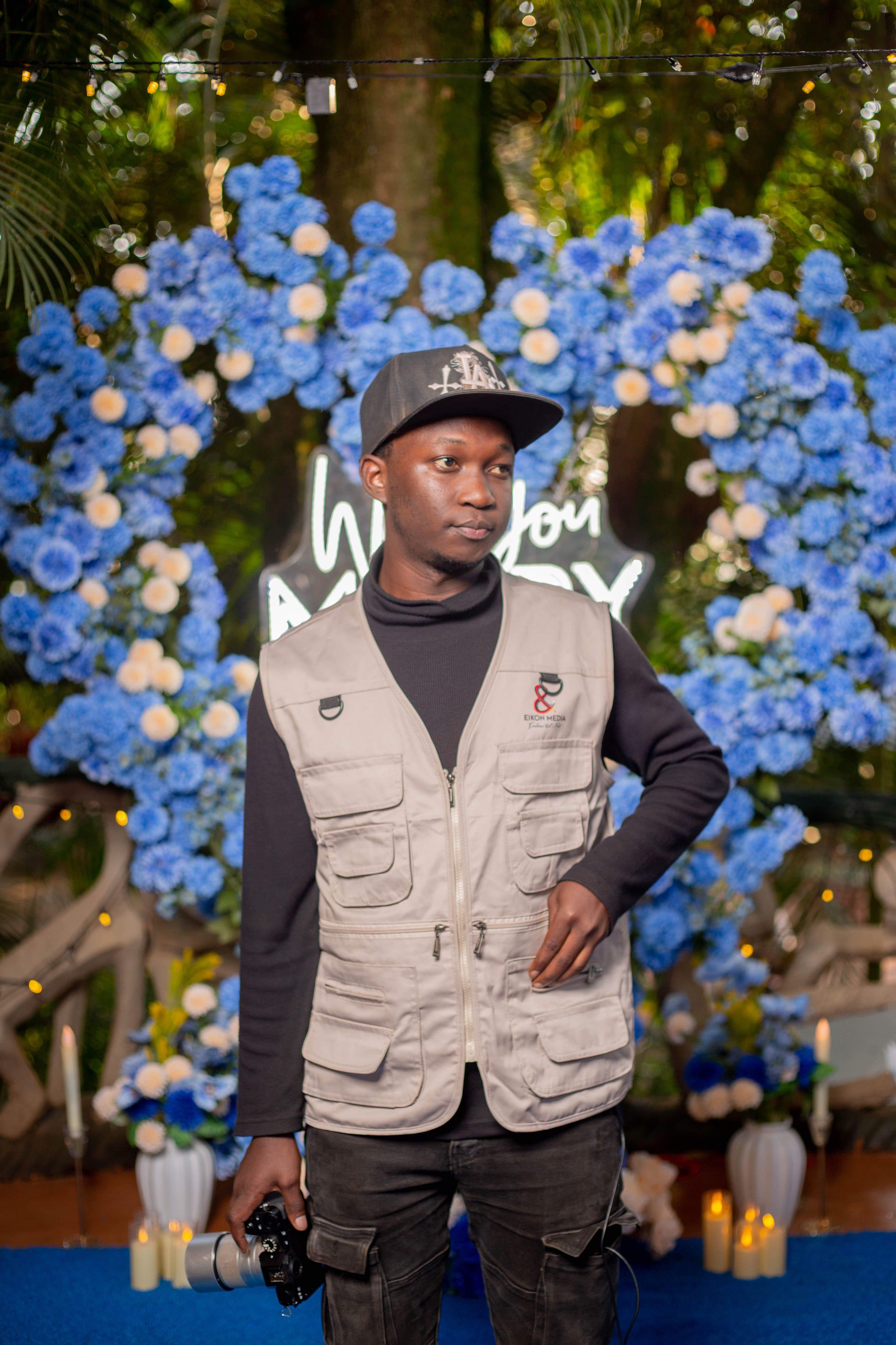 Photographer posing in front of vibrant blue floral backdrop during an event.