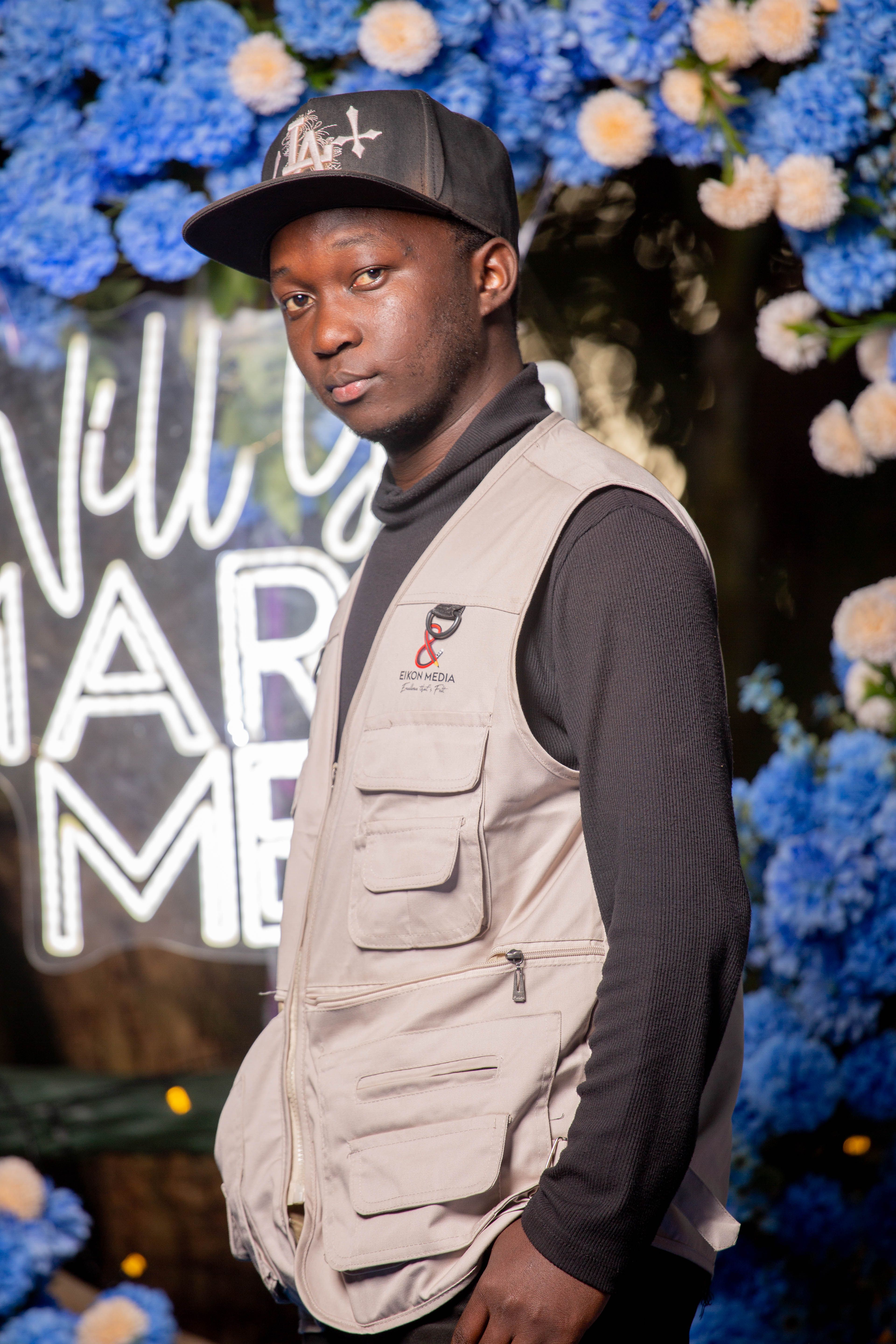 A young man stands confidently in front of a vibrant floral arrangement.