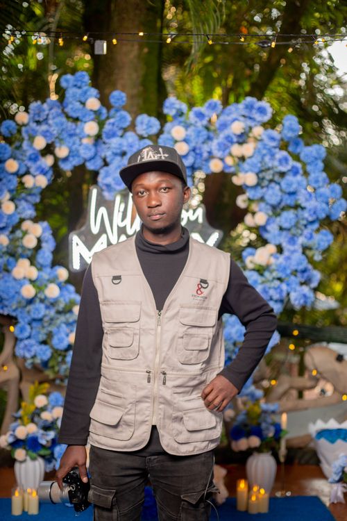 Free Man standing in front of floral arrangement at outdoor event, holding a camera. Stock Photo