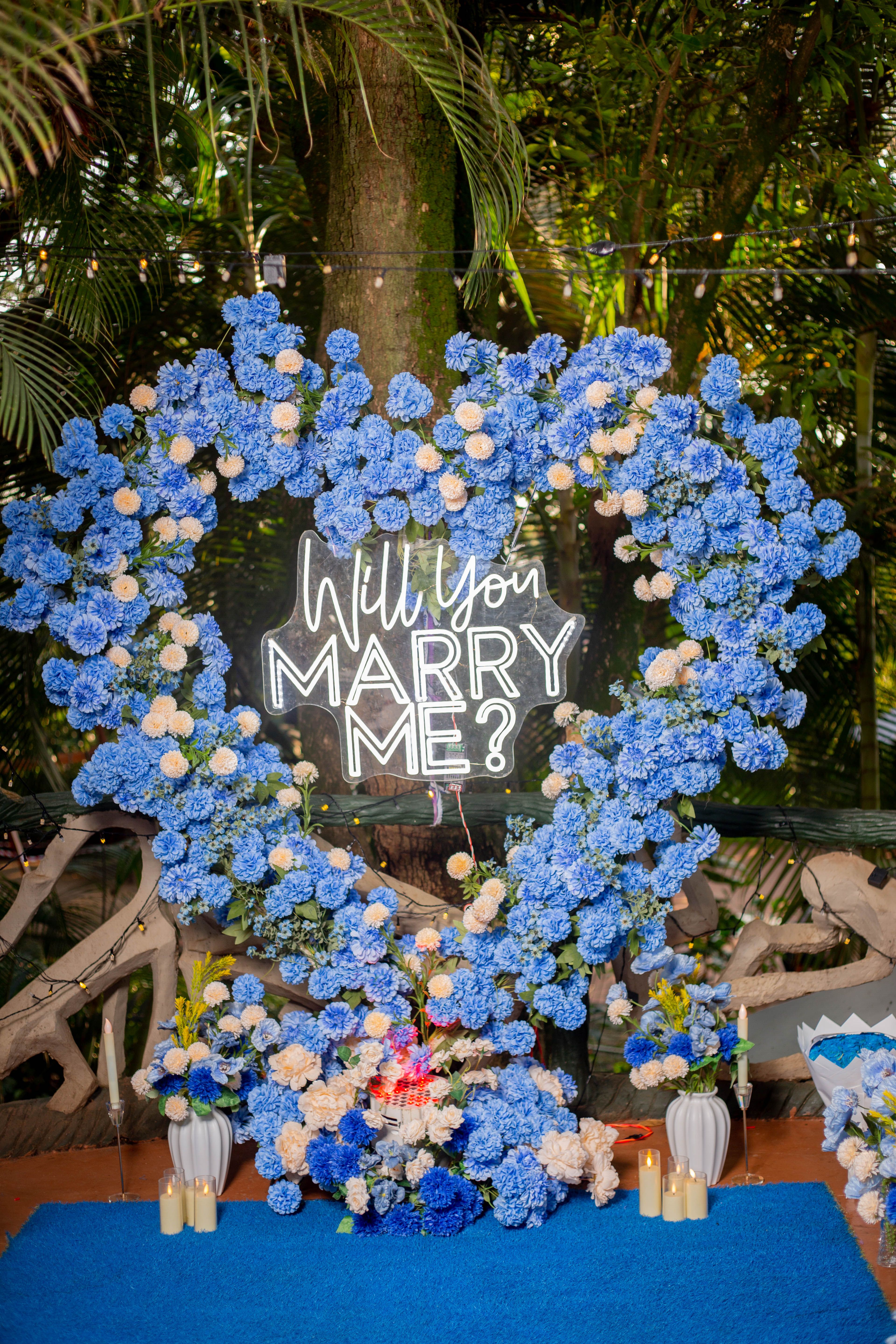 Beautiful proposal scene with heart-shaped blue flower arrangement and candles.