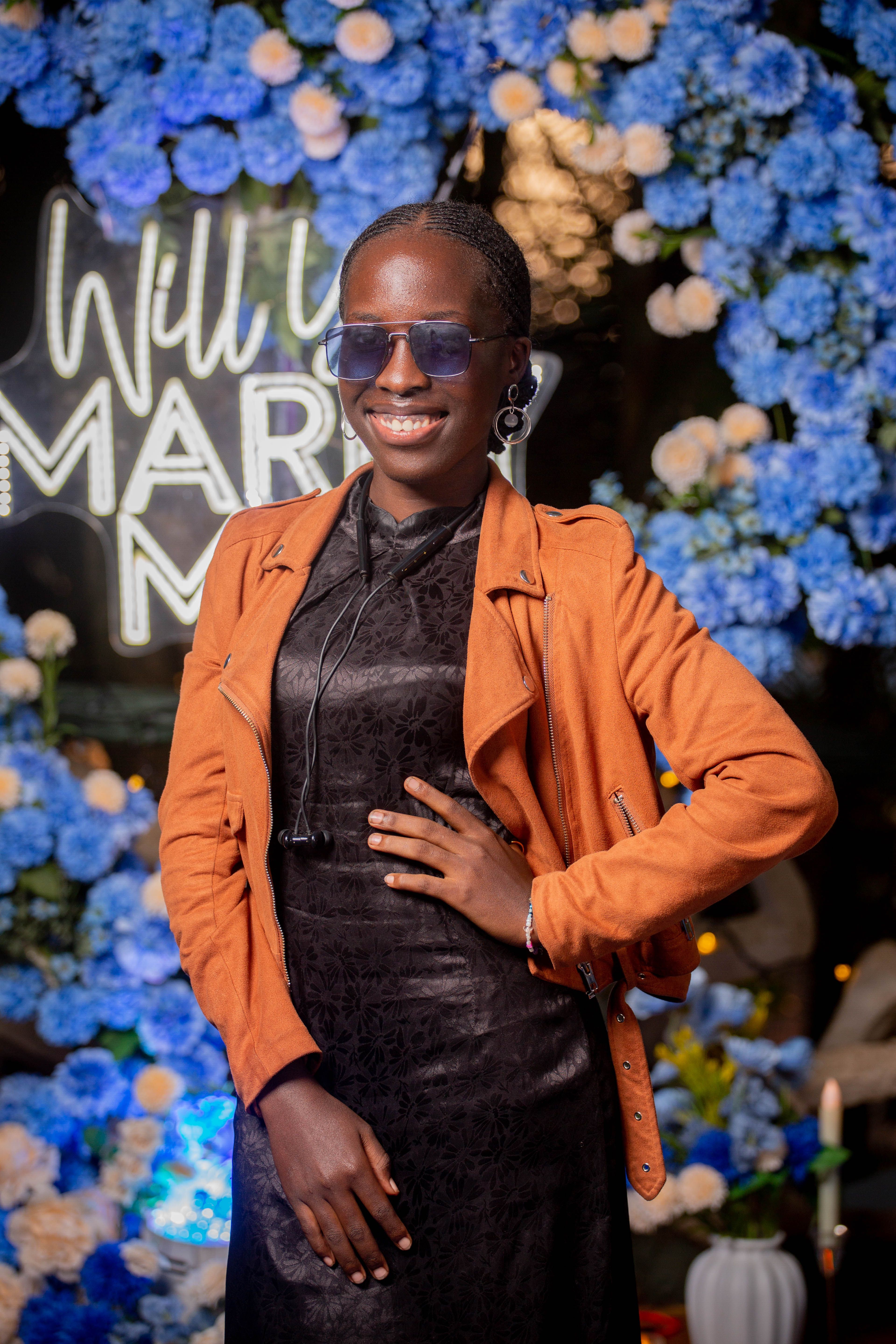 Confident woman with sunglasses poses at a vibrant floral engagement event.