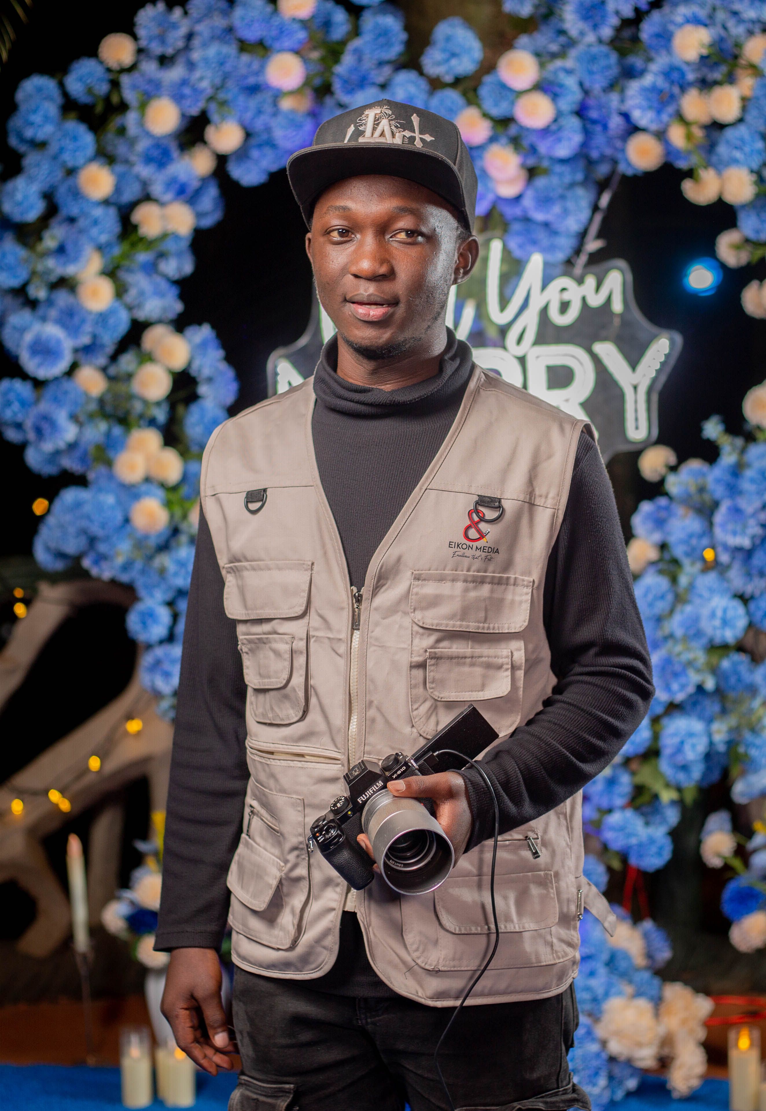 Young photographer holding a camera against a vibrant flower backdrop, capturing an elegant event atmosphere.