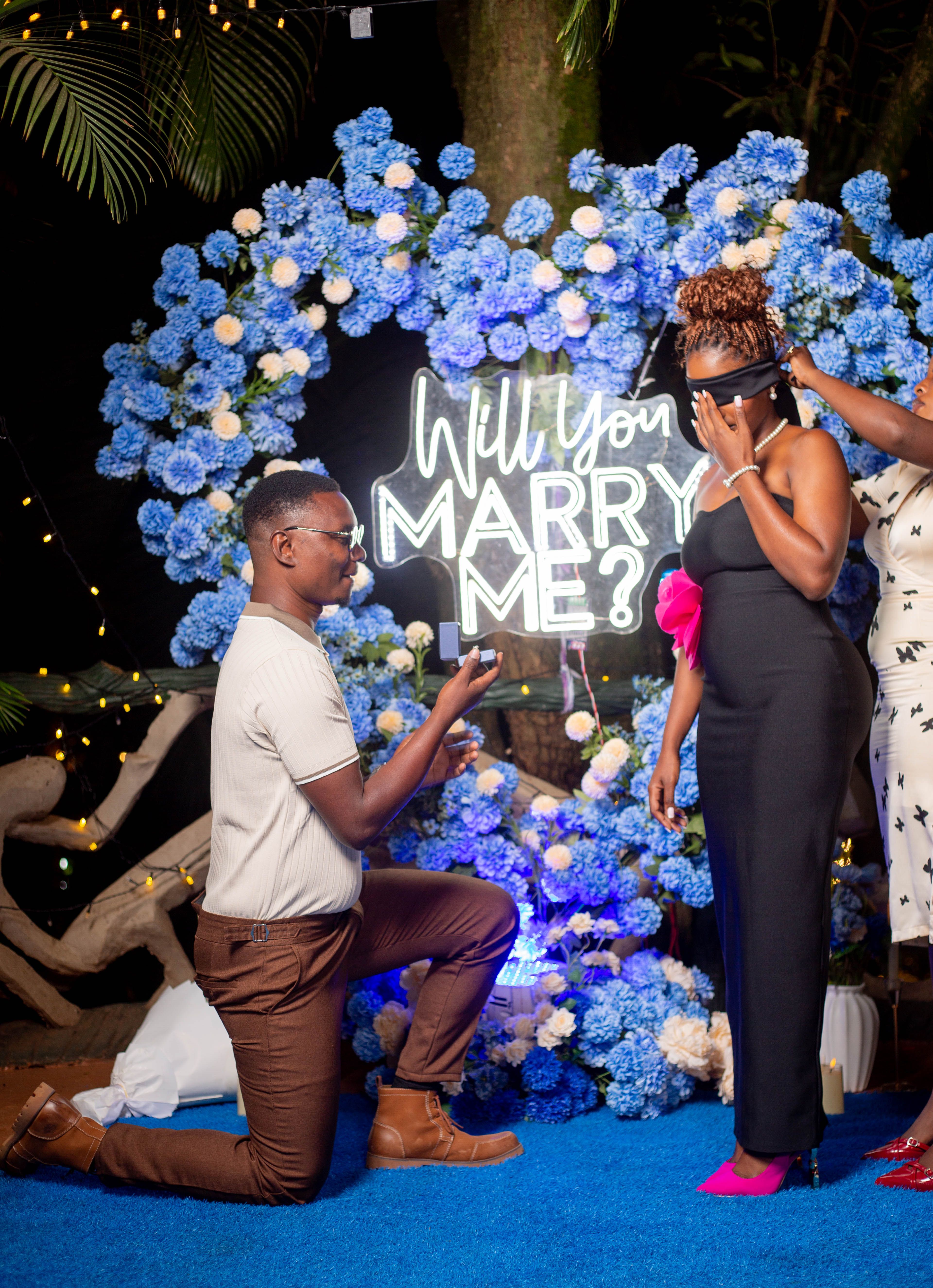A heartfelt marriage proposal with a floral backdrop and glowing neon sign under night sky.