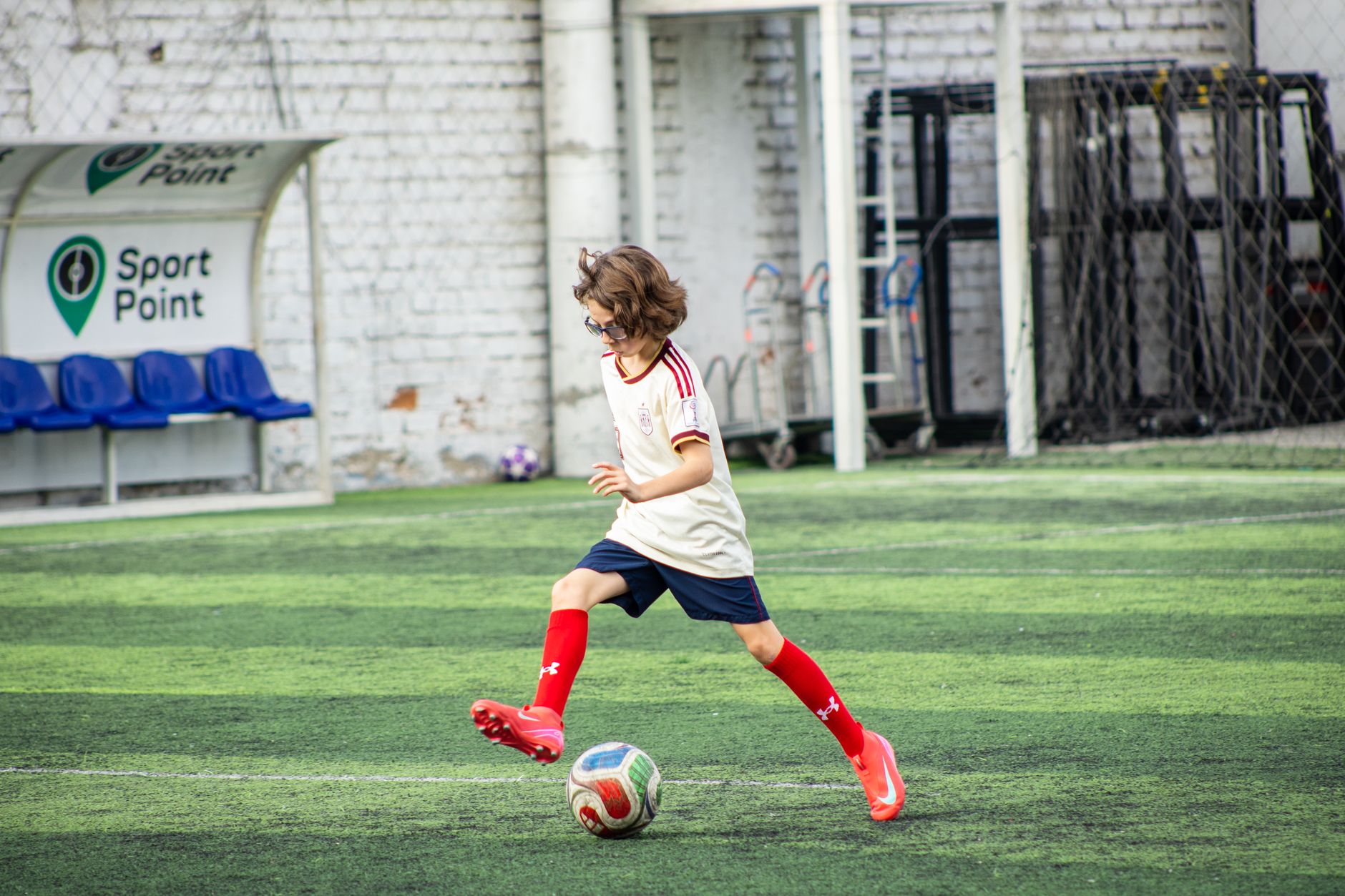 Young boy playing soccer on a sports field, wearing red socks and focused on the game.