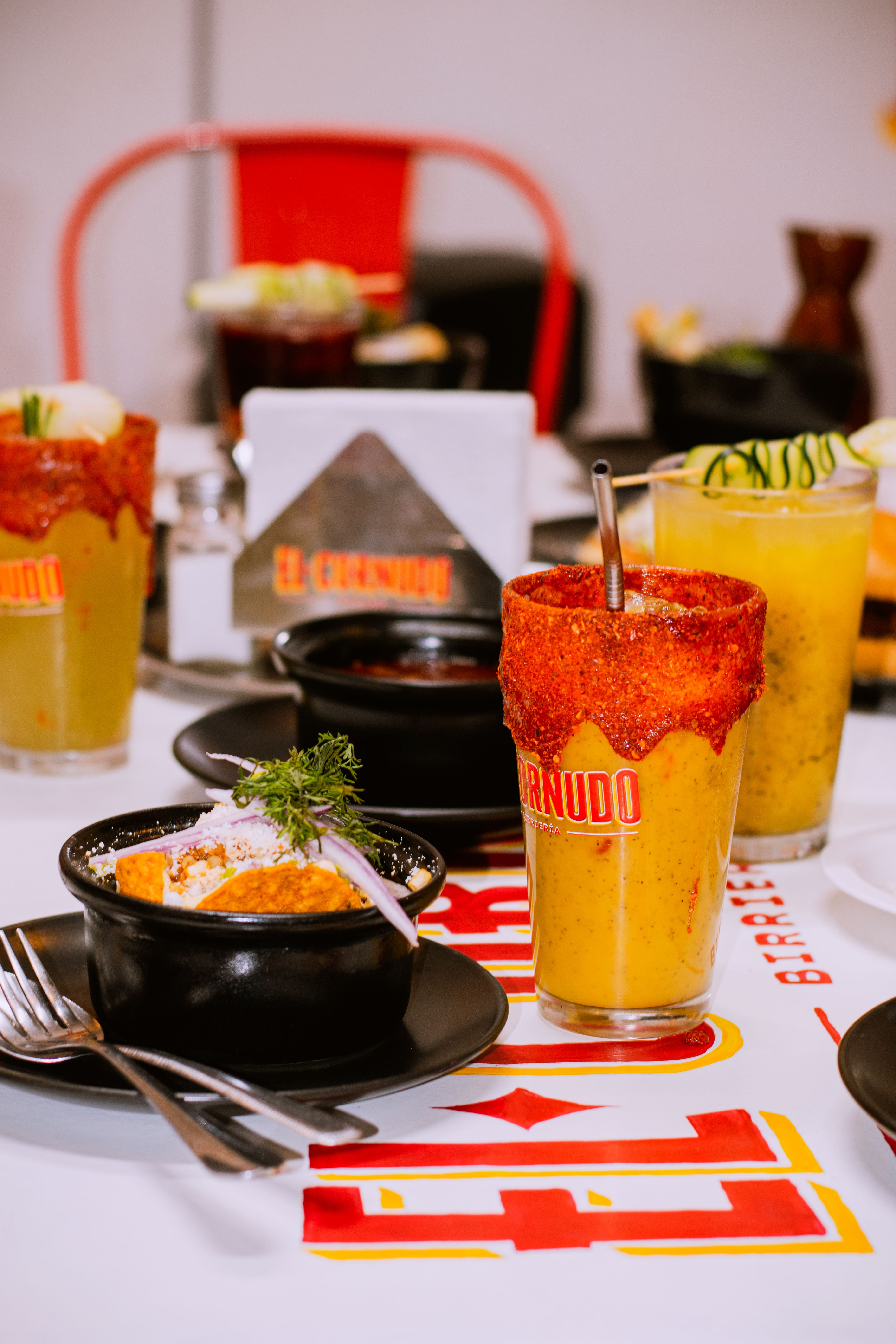 Colorful Mexican drinks and dishes on a table in a lively restaurant setting.