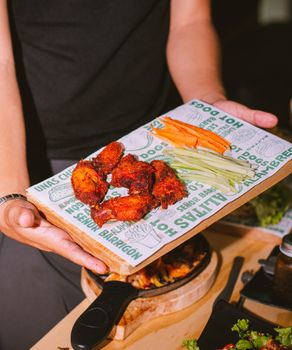 Spicy chicken wings served with carrot and celery sticks on a wooden board.