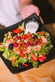Colorful salad with fresh berries, nuts, and dressing served on a black plate.
