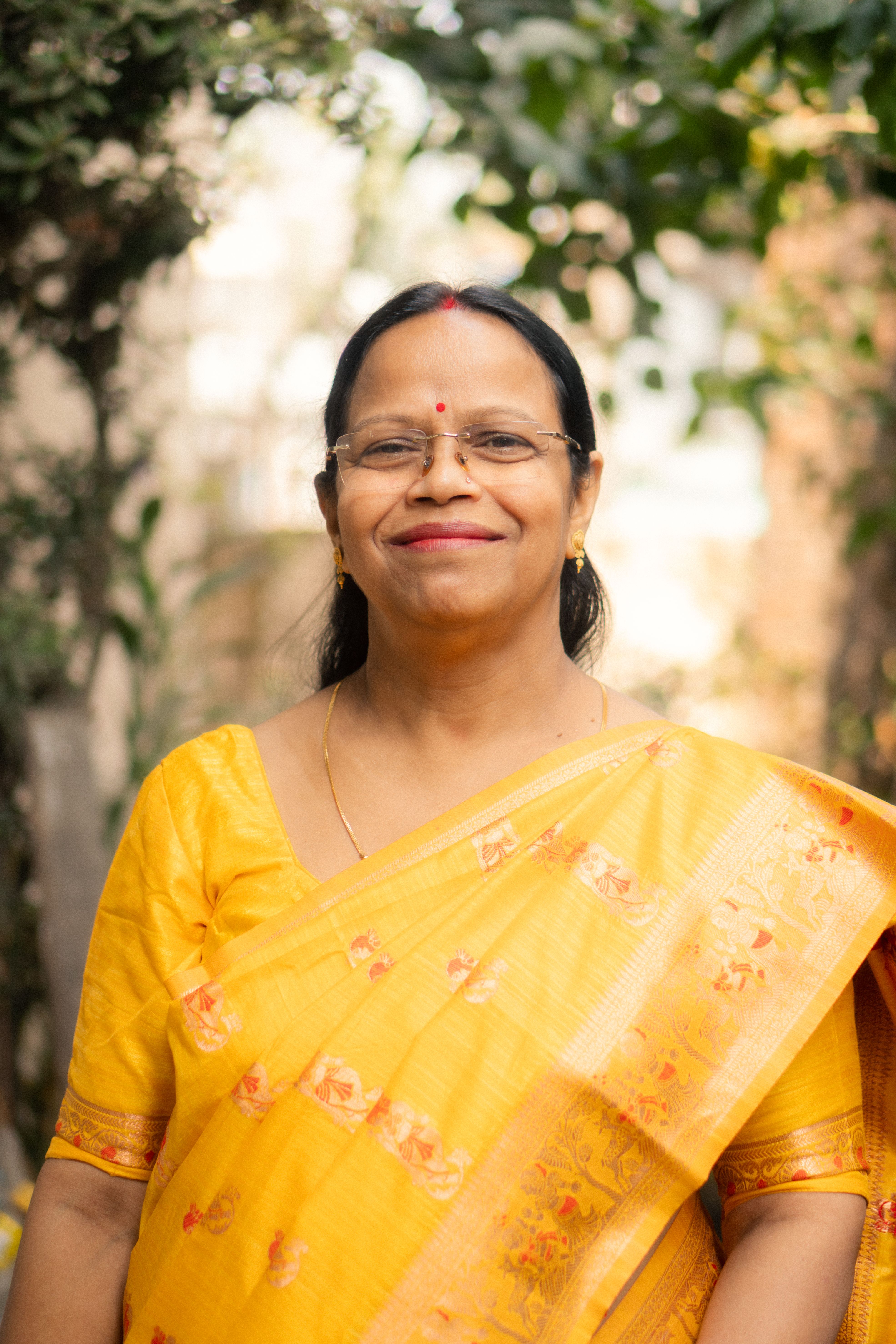 Cheerful woman in yellow saree standing outside, exuding warmth and culture.