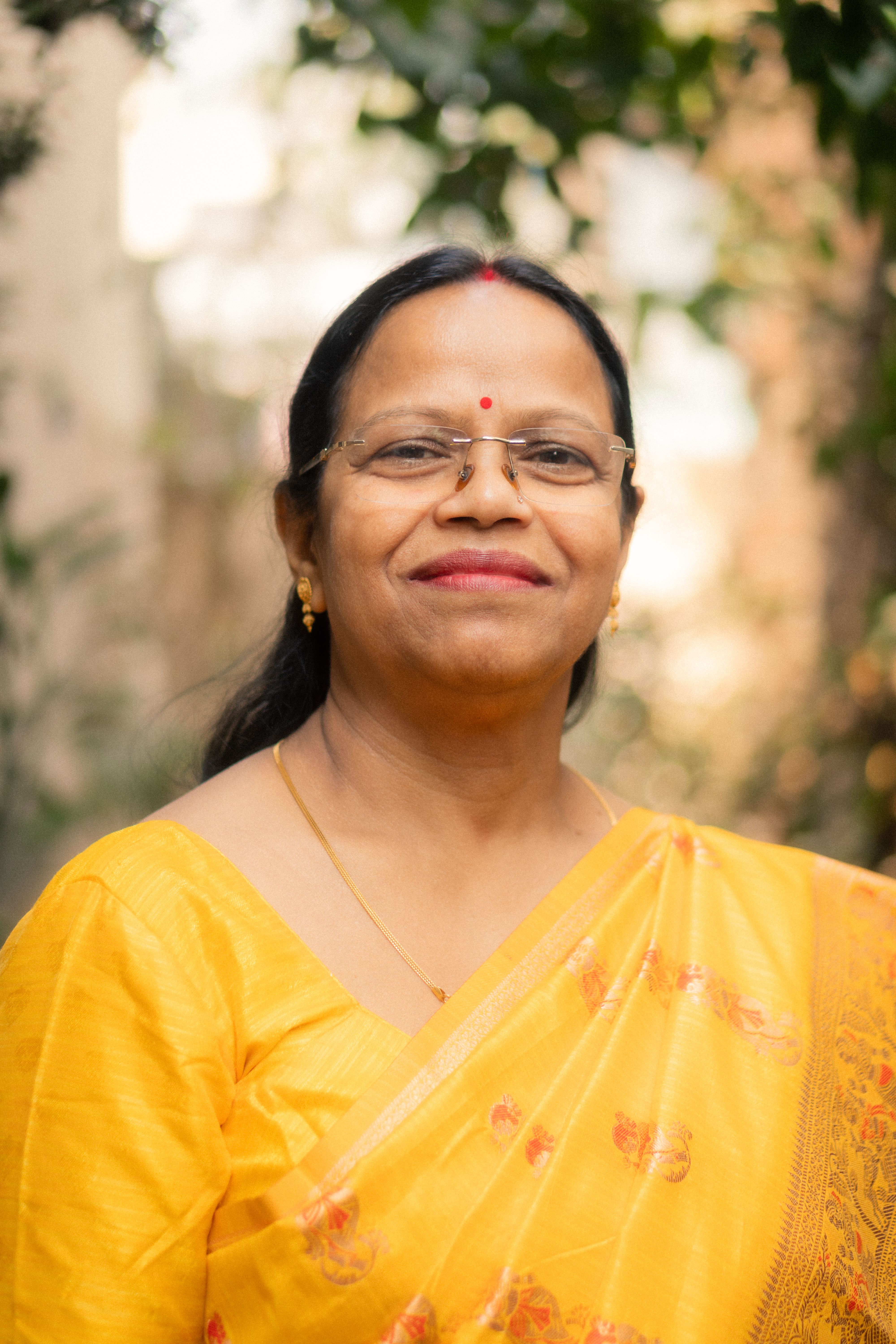 A joyful woman wearing a yellow saree with floral designs standing outdoors.